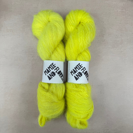 Two bright yellow skeins of yarn with labels on a beige background